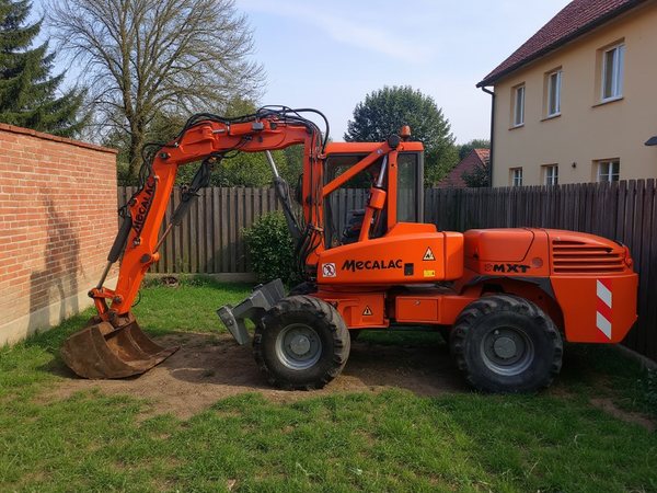 Koparka kołowa Mecalac pracuje przy ścianie domu w ogrodzie